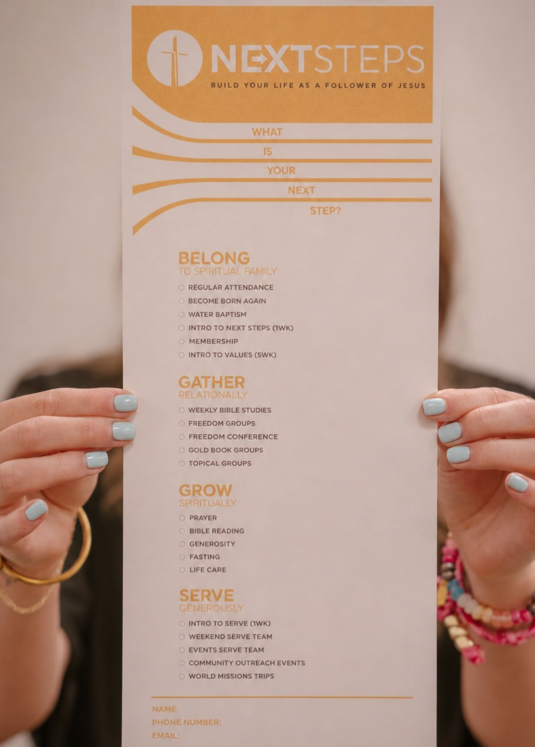 A guest holding up a Next Steps card showing ways to belong, gather, grow, and serve